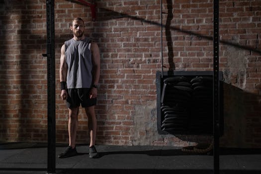 A muscular athlete in activewear stands by a brick wall in a gym, casting a shadow.