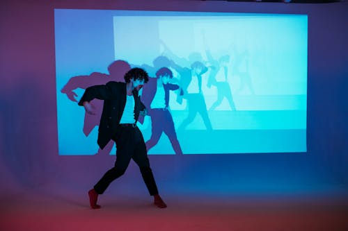 Man in Black Suit Dancing With A Projector Screen Behind Him