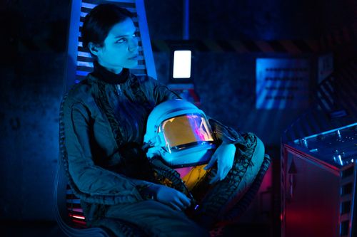 Free Astronaut in a blue-lit futuristic setting holding a helmet, signifying space travel. Stock Photo
