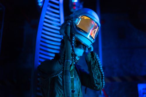 Free Astronaut in a futuristic suit adjusts helmet in a blue-lit sci-fi setting. Stock Photo