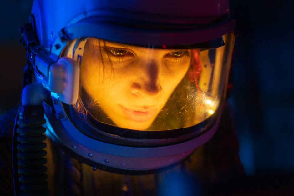Uzayda astronot benzeri figür, mavi ışık altında düşünceli duruyor