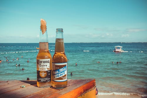 Two Corona Extra and San Mig Light Beers on Top of Brown Wooden Plank Near Beach