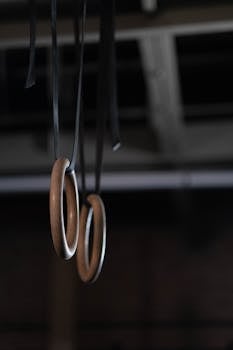 Wooden gymnastic rings hanging in a dimly lit gym, capturing a moody atmosphere.