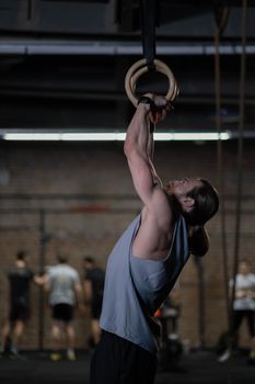 Athletic man performing exercises on gymnastic rings in a gym setting, showcasing strength and fitness.