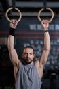 Man in Gray Tank Top Holding onto Gymnastic Rings