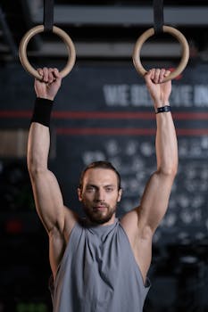 A male athlete performing strength training exercises on gymnastic rings in a gym setting.