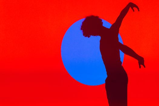 A silhouette of a ballet dancer performing against a vibrant red and blue abstract background.