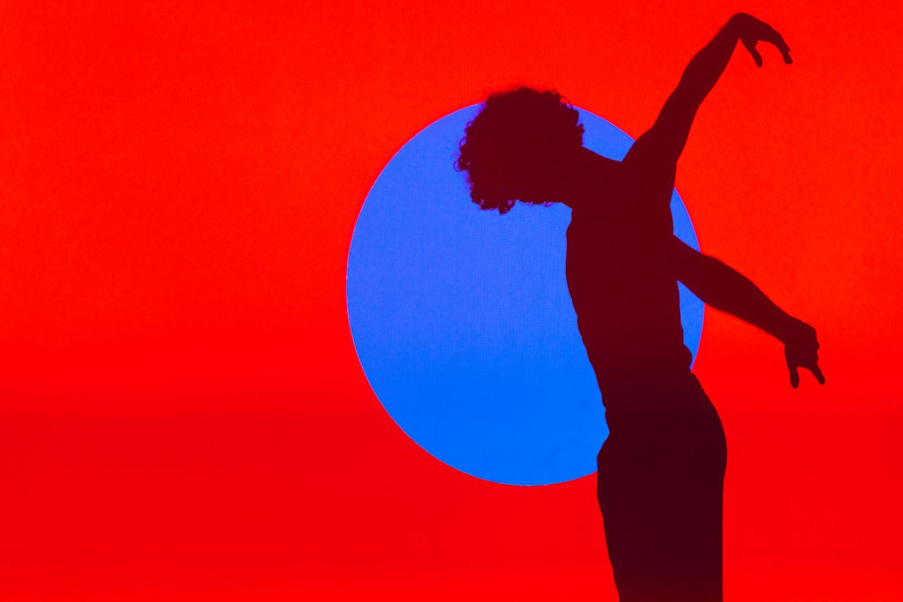 a silhouette of a ballet dancer performing against a vibrant red and b