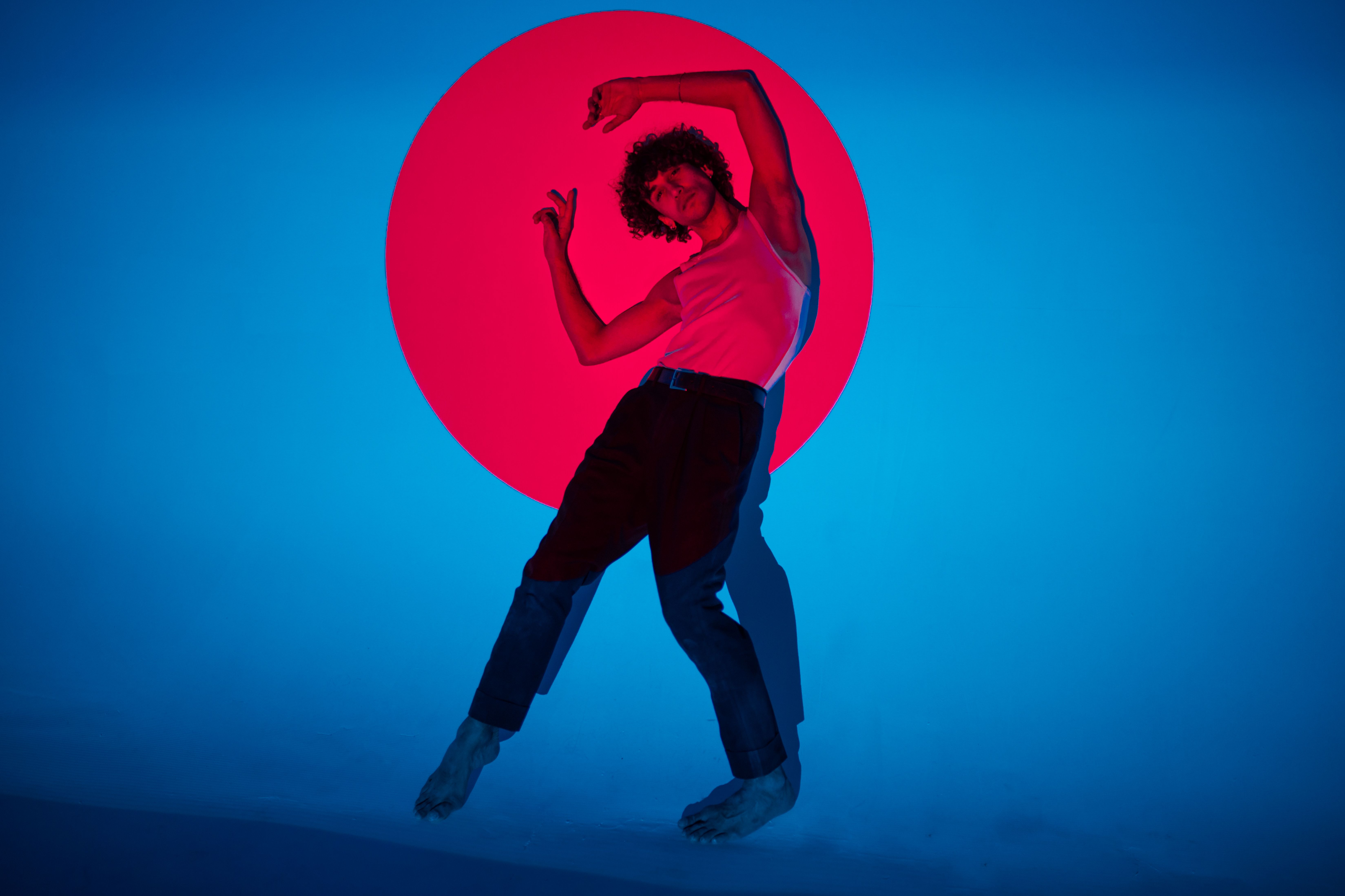 A contemporary dancer poses dynamically against a vibrant blue and red background in a studio setting.