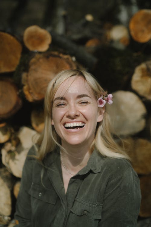 A Smiling Woman in Black Shirt With Flowers Tuck on Her Ear