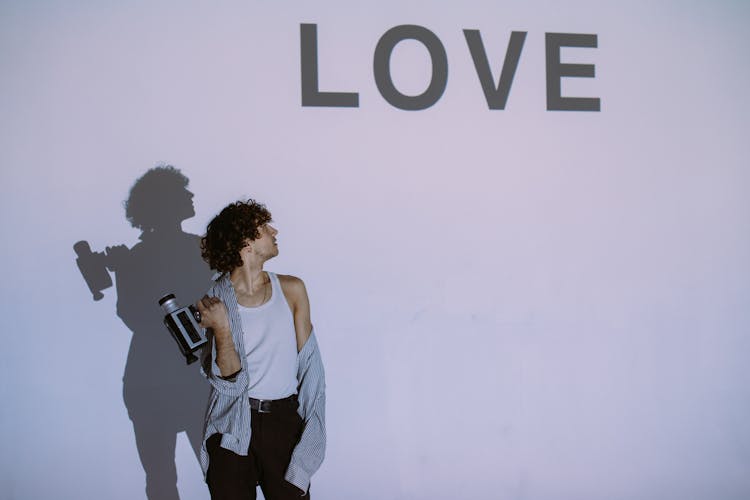 Man Holding A Camera And Looking On A Love Sign On Wall