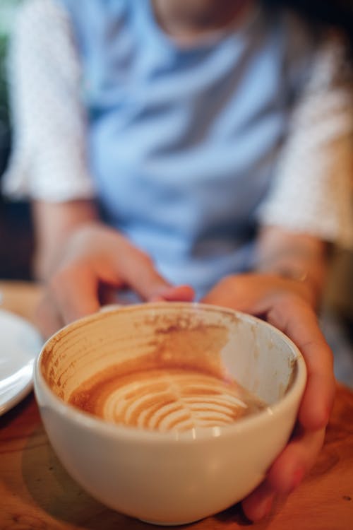 Free Soft focus of crop unrecognizable female sitting at table with cup of hot coffee with latte art in light cafe Stock Photo
