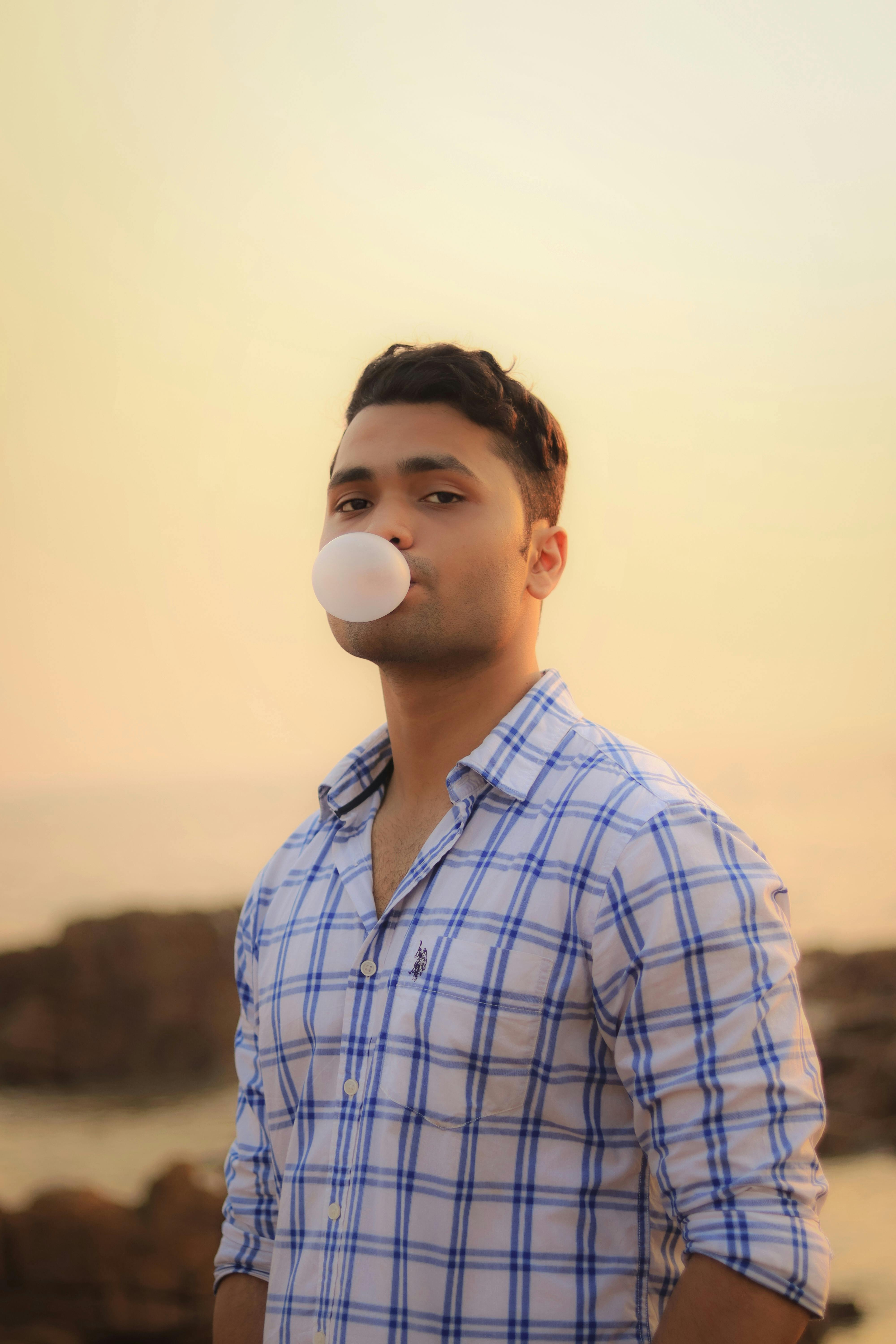 Man in plaid blowing bubble gum outdoors at sunset, capturing a playful moment.