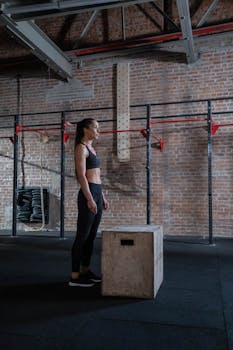 Woman in activewear preparing for a box jump in industrial-style gym.