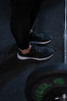 Close-up of black sneakers and barbell on gym floor, perfect for fitness themes.