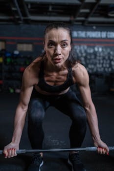 Focused woman lifting a barbell in a gym setting, showcasing strength and determination.