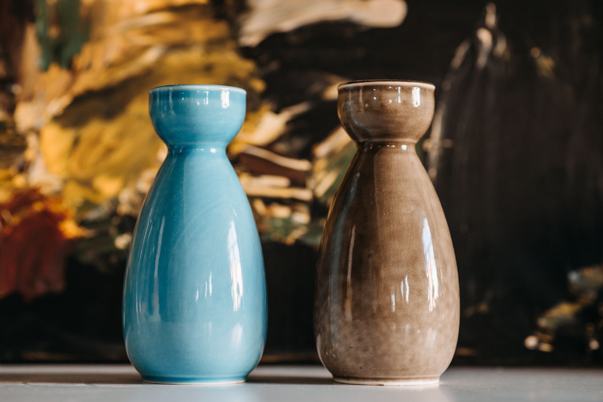 Two glazed ceramic vases in blue and brown against an abstract backdrop.