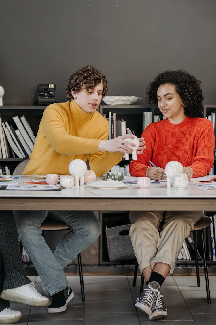 Young Man And Woman Sitting At The Table With Variety Of Ceramic Products 