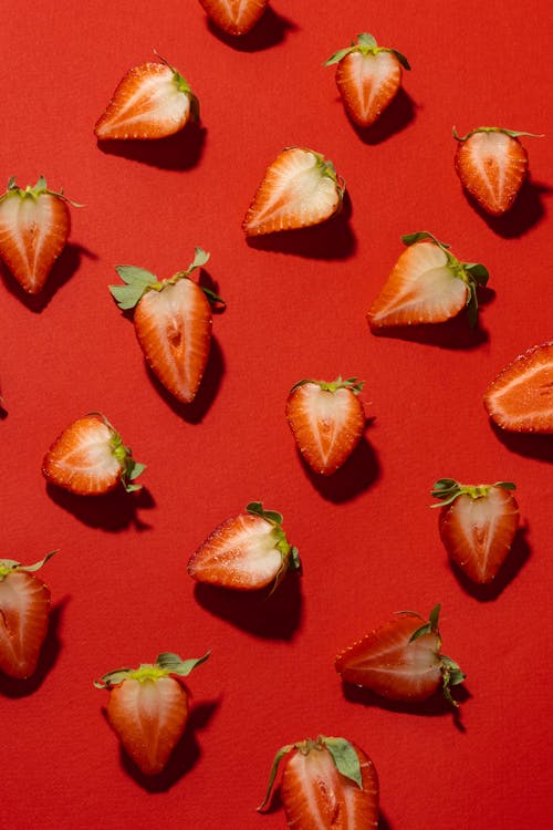 Strawberries Cut in Half Lying on Red Background 