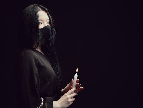 Free A Woman in Black Top Wearing Face Mask Holding a Candlelight Stock Photo