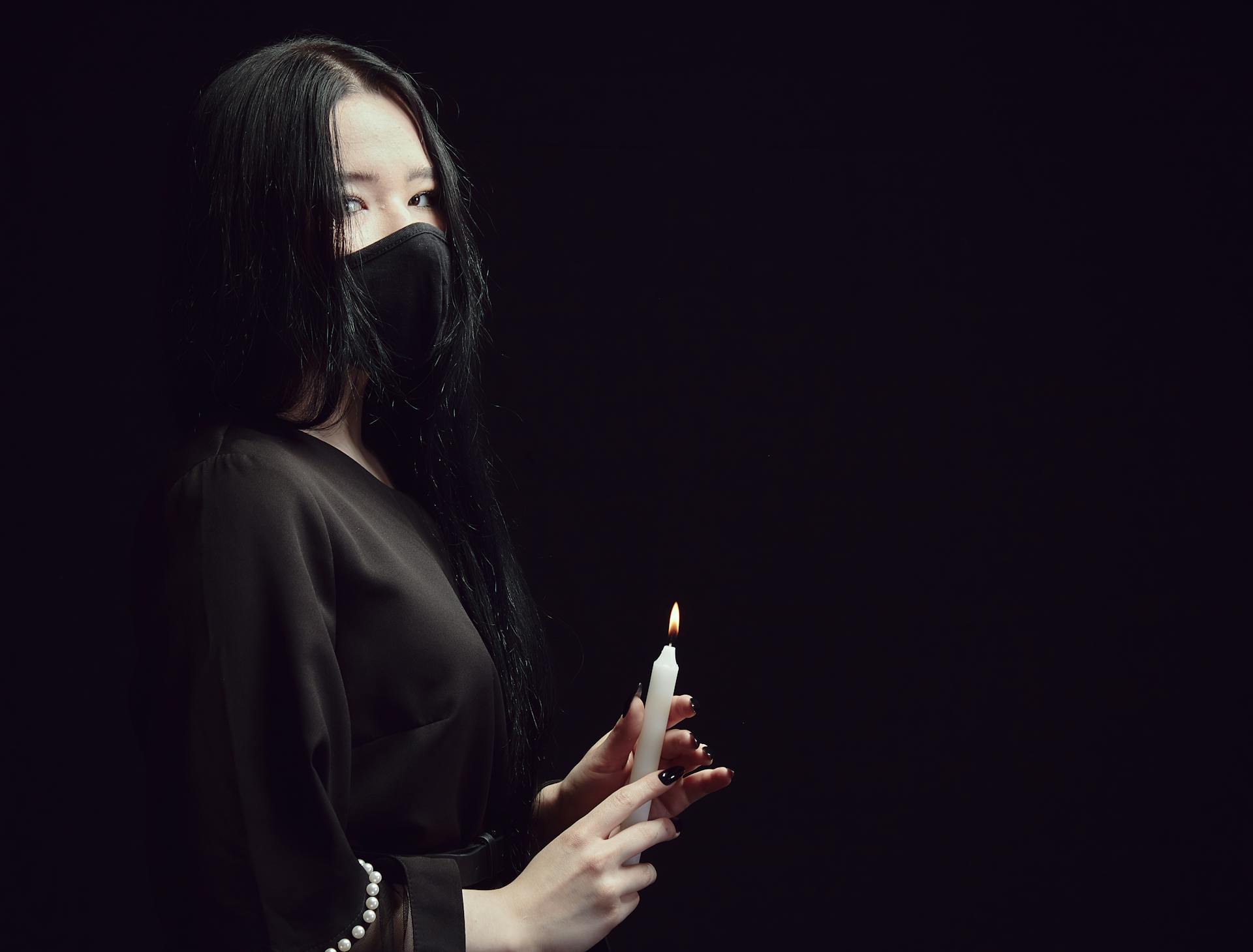 A Woman in Black Top Wearing Face Mask Holding a Candlelight