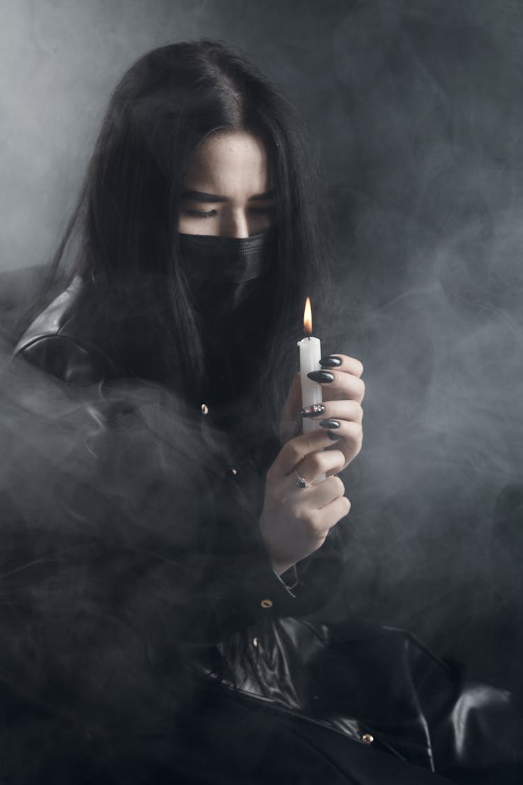 A Woman In Black Facemask Holding A Lighted Candle