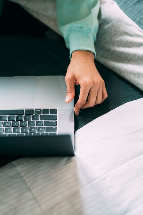 Free From above of crop unrecognizable male freelancer surfing internet on netbook while sitting on comfortable bed in bedroom at home Stock Photo