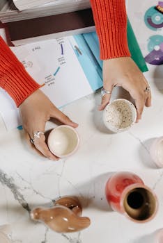 Hands arranging ceramic jars on marble, showcasing pottery skills.