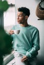 Thoughtful black man with cigarette drinking coffee near window