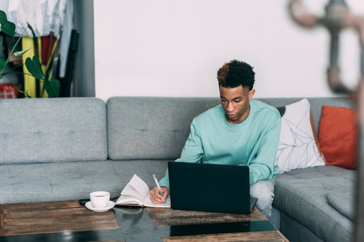 Thoughtful Black Man With Laptop Writing In Notebook