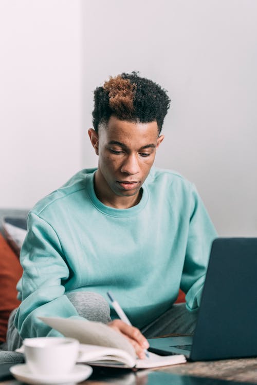 Thoughtful black man taking notes near laptop