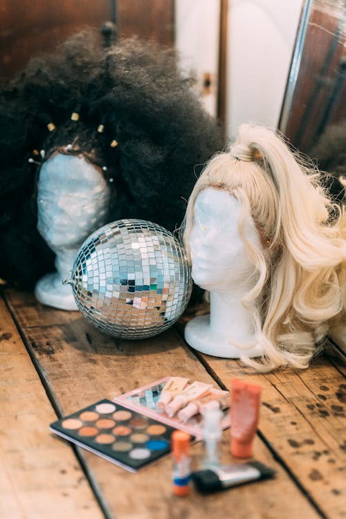 Wigs on mannequins near sparkling disco ball and palette