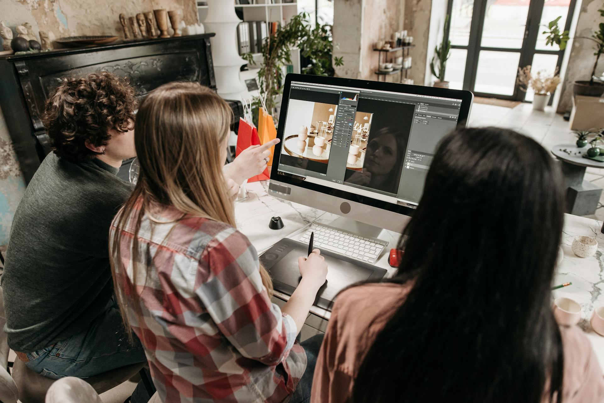 A group of young adults working on a design project using a desktop computer in an artistic workspace.