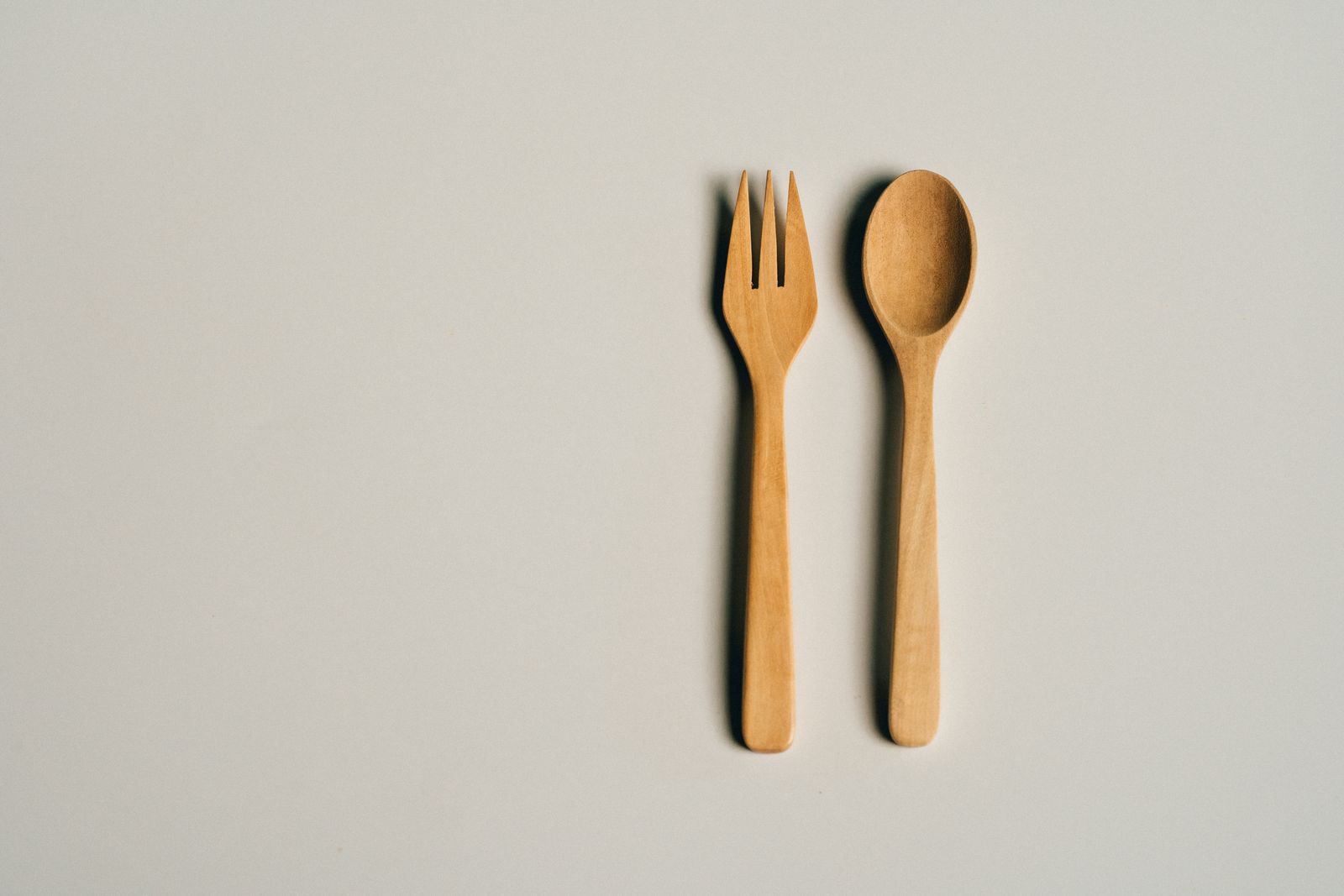 Simple and elegant wooden fork and spoon set on a soft gray background, perfect for culinary and lifestyle themes.