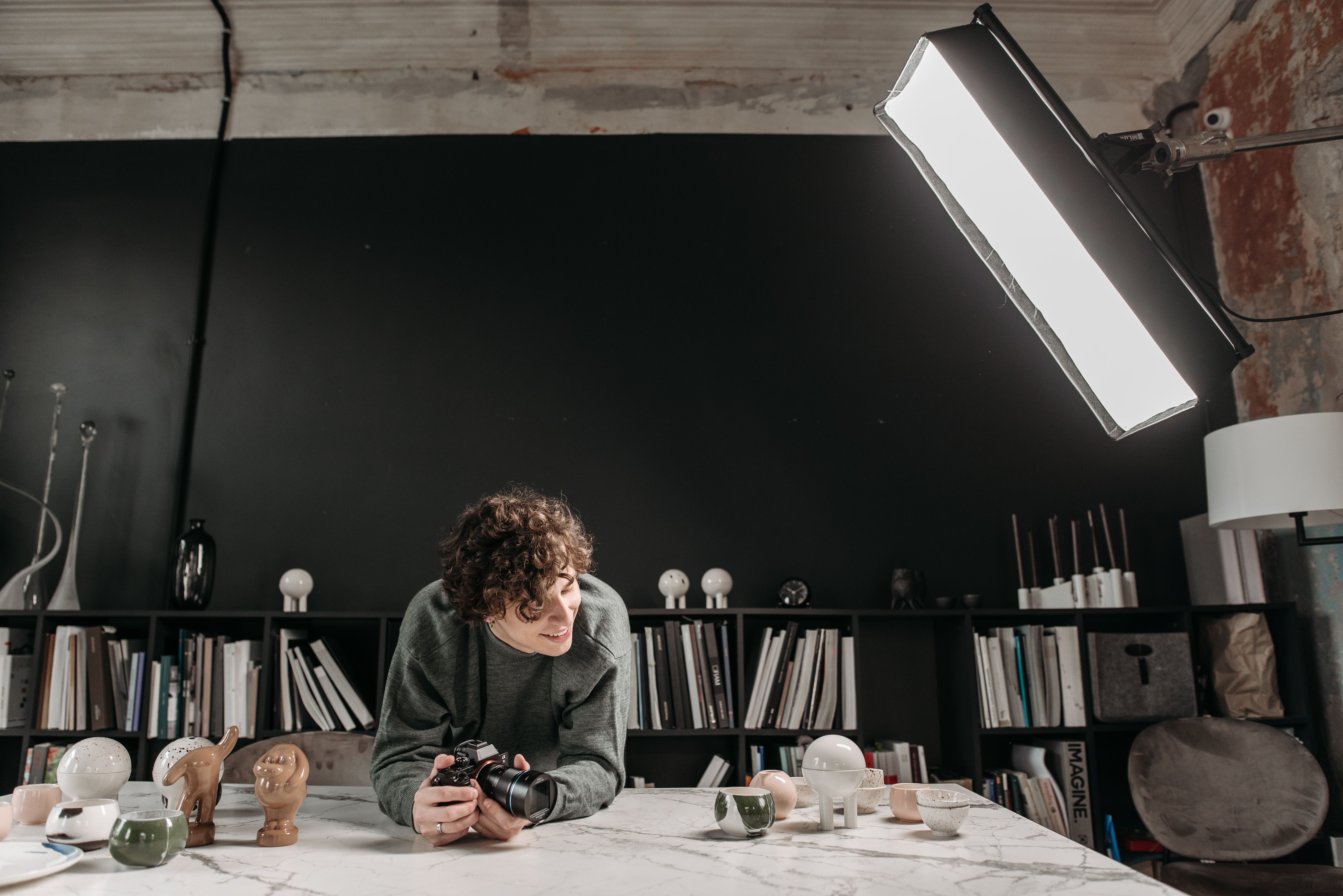 Free Male photographer in a creative studio surrounded by ceramics, books, and lighting equipment. Stock Photo