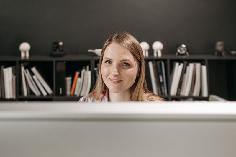 Friendly young woman at her desk with bookshelves in modern office setting