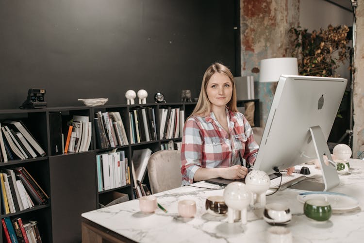 Woman In Red Plaid Shirt Sitting And Working In Front Of A Desktop Computer Inside An Office 