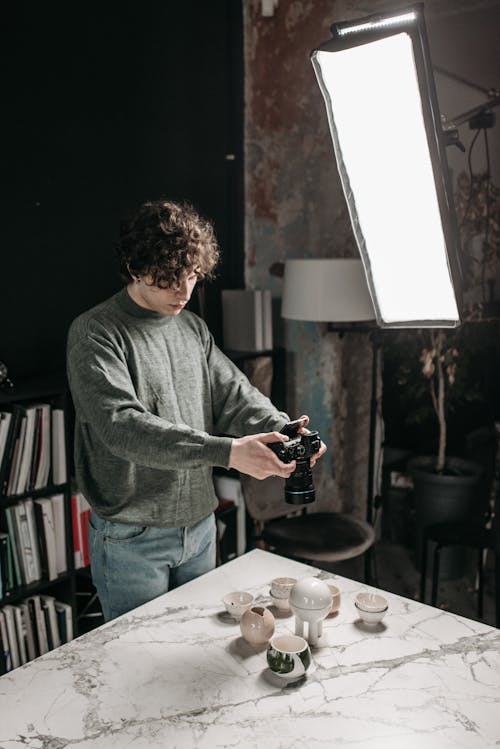 A Man in Gray Sweater Taking Photo of Ceramic Products