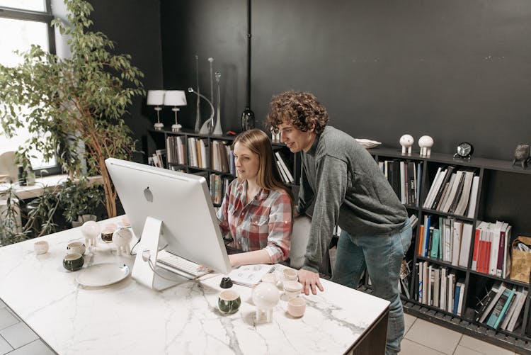 Young Coworkers Working And Talking In Front Of A Desktop Computer On A Ceramic Table