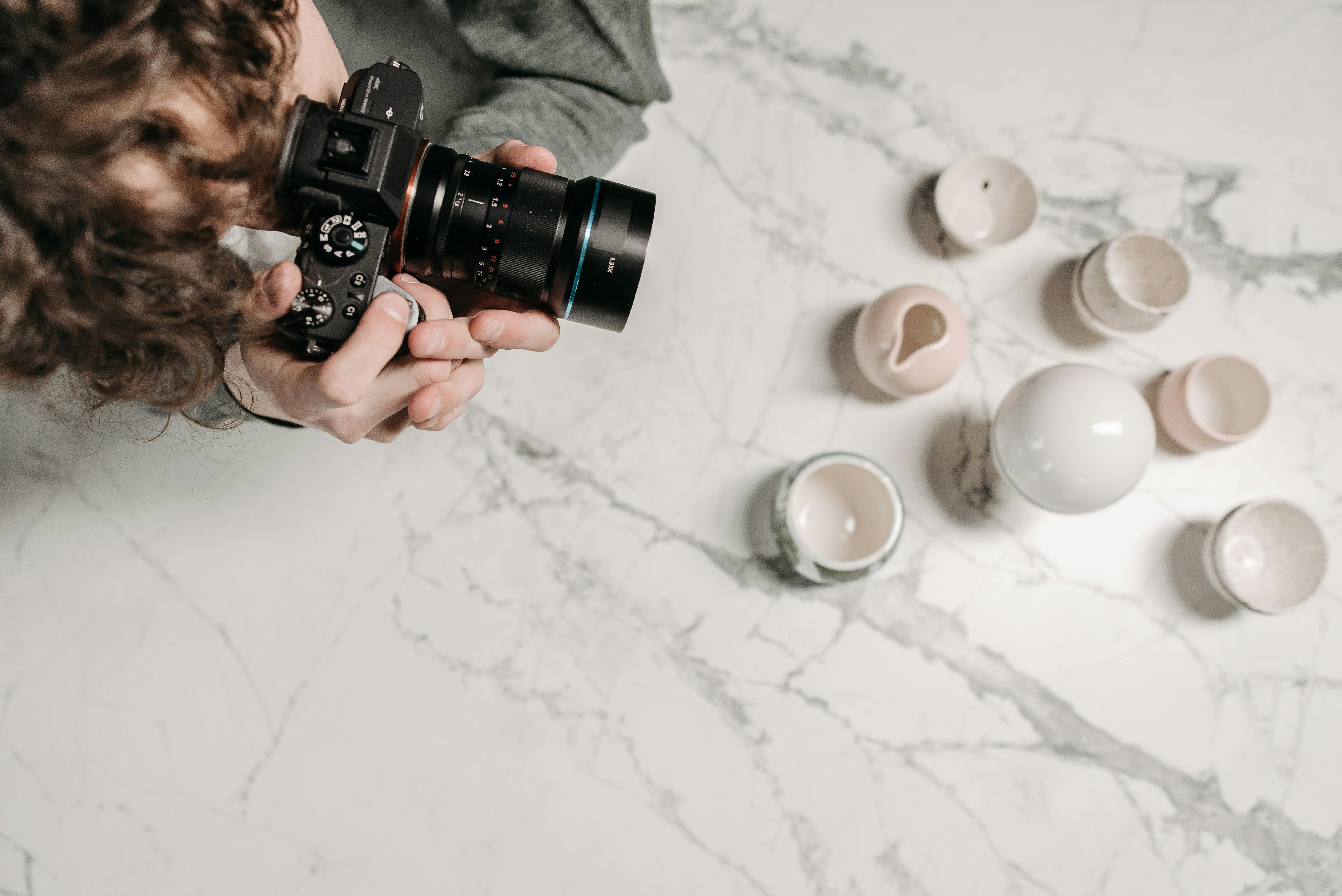 Man photographing ceramic cups on marble surface from above, indoors.