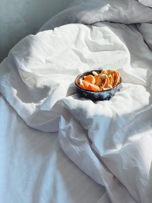 Free High angle bowl with fresh ripe fruits and sweet pancakes served on comfortable bed with soft white blanket in sunny morning Stock Photo