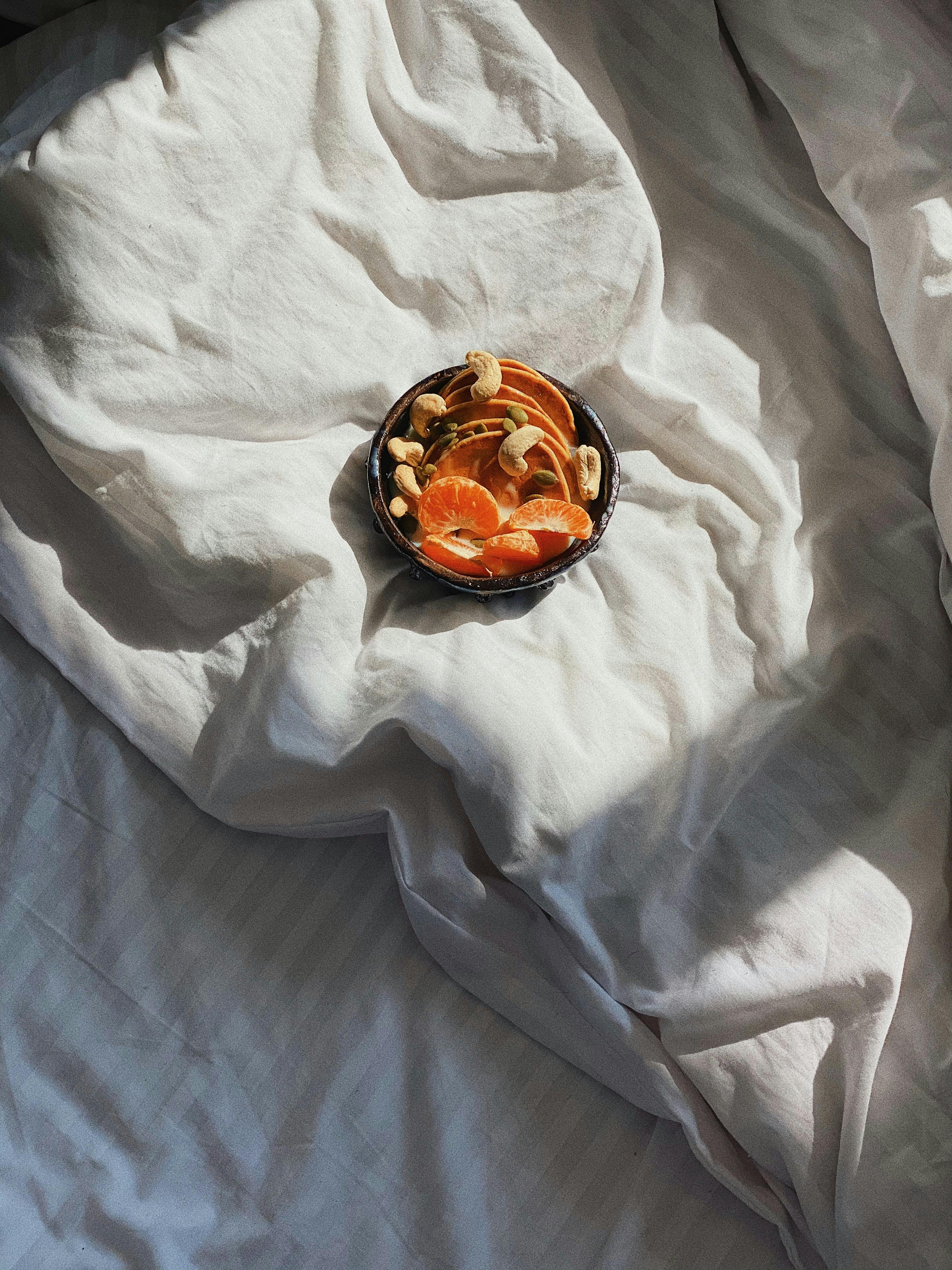 Inviting breakfast bowl with oranges and nuts on a sunlit bed, offering a cozy morning vibe.