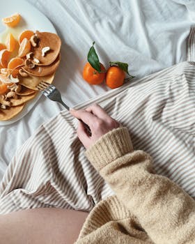 A cozy breakfast scene featuring pancakes with nuts and fresh tangerines on a soft bed setting.