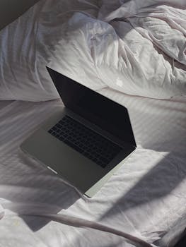 A laptop is placed on a sunlit bed, creating a cozy and tranquil ambiance at home.
