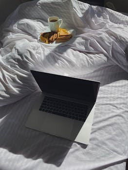 Laptop and breakfast on a sunny bed, creating a cozy start to the day.