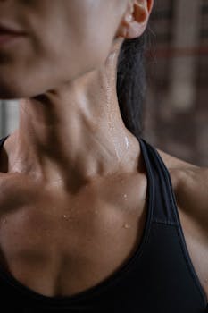 Close-up of a fit woman in activewear glistening with sweat, showcasing toned muscles.