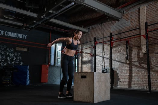 A fit woman performing a box jump in an industrial-style gym setting. Ideal for fitness themes.