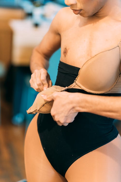 Crop unrecognizable black woman in bodysuit touching breast against mirror  · Free Stock Photo