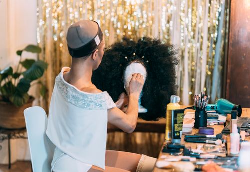 Free Side view of anonymous female in white outfit and hairnet sitting at table with cosmetics while holding wig stand with Afro wig Stock Photo