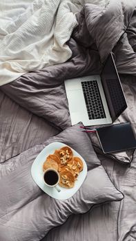 Relaxed morning setup with pancakes and coffee on bed alongside a laptop and notebook.